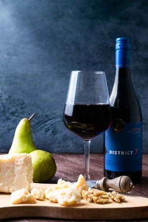 Glas med rött vin, ost, nötter och en flaska rött